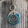 foto di un ciondolo rotondo color turchese in ceramica raku con una spirale in metallo