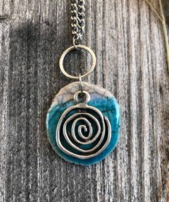 foto di un ciondolo rotondo color turchese in ceramica raku con una spirale in metallo